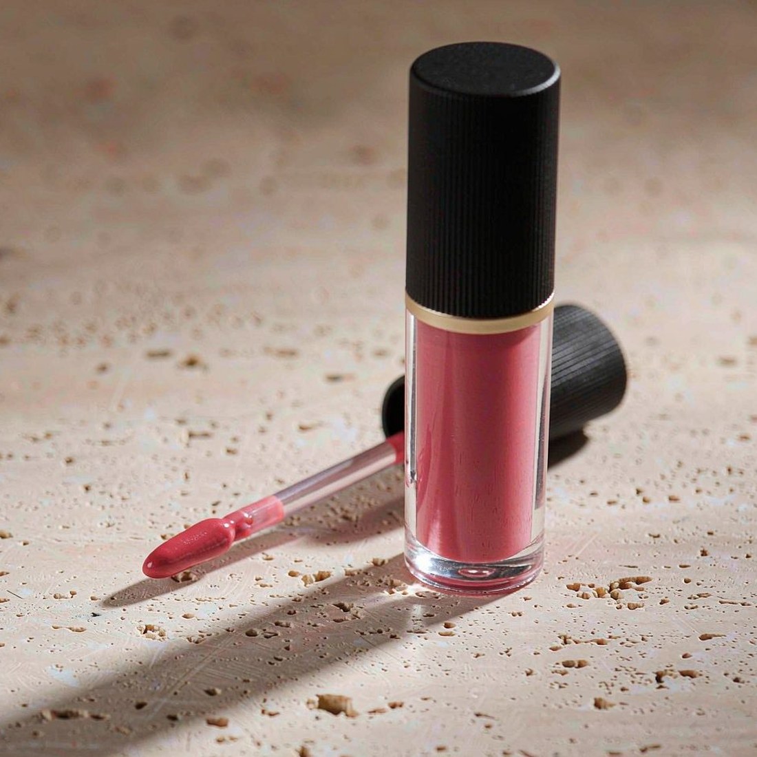 Transparent lip gloss tube with rose-pink formula and matte black cap
