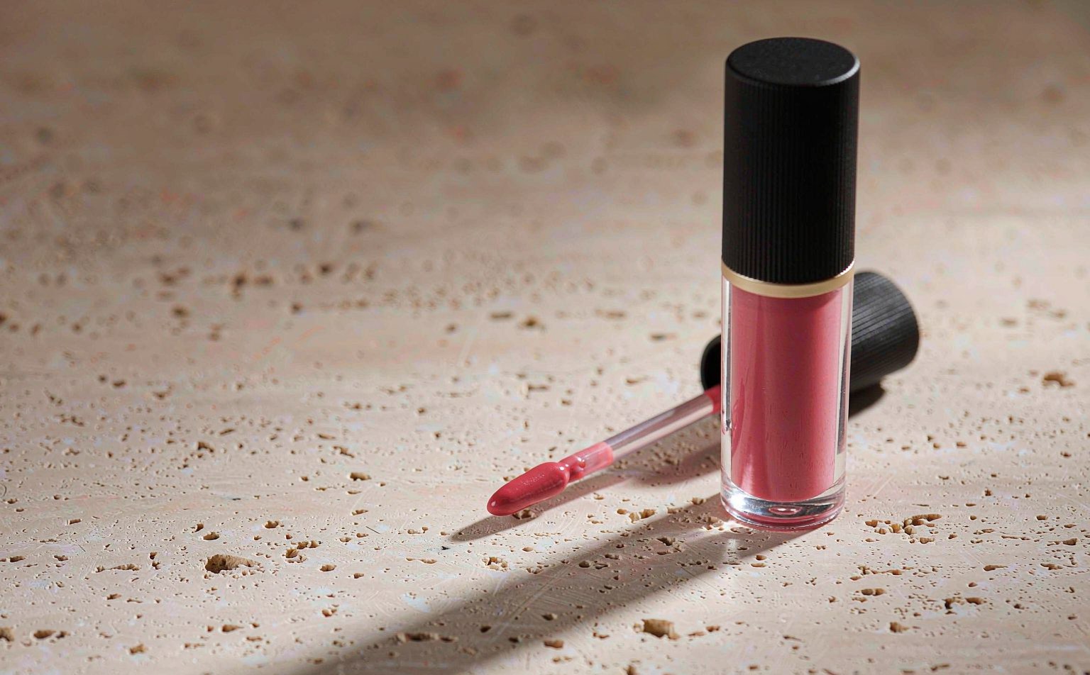 Transparent lip gloss tube with rose-pink formula and matte black cap